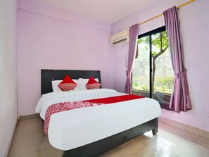 A bedroom with a bed, an air conditioning unit, a window with curtains, and a view of greenery outside. - OYO 91680 Hotel MentariNearRumah Sakit Myria (Palembang)