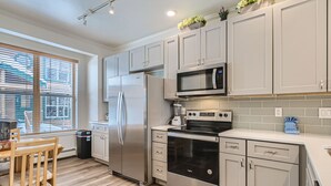 A modern kitchen with stainless steel appliances, light-colored cabinetry, and a wooden dining table. - 2-BD 3-BDR Ski Cabin (Silverthorne)