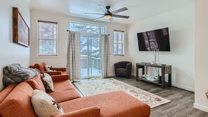 A living room with a sofa, a television, a ceiling fan, and a view of the outdoors. - 2-BD 3-BDR Ski Cabin (Silverthorne)