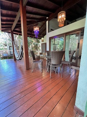 A covered outdoor area with wooden flooring, wicker furniture, and hanging lamps.