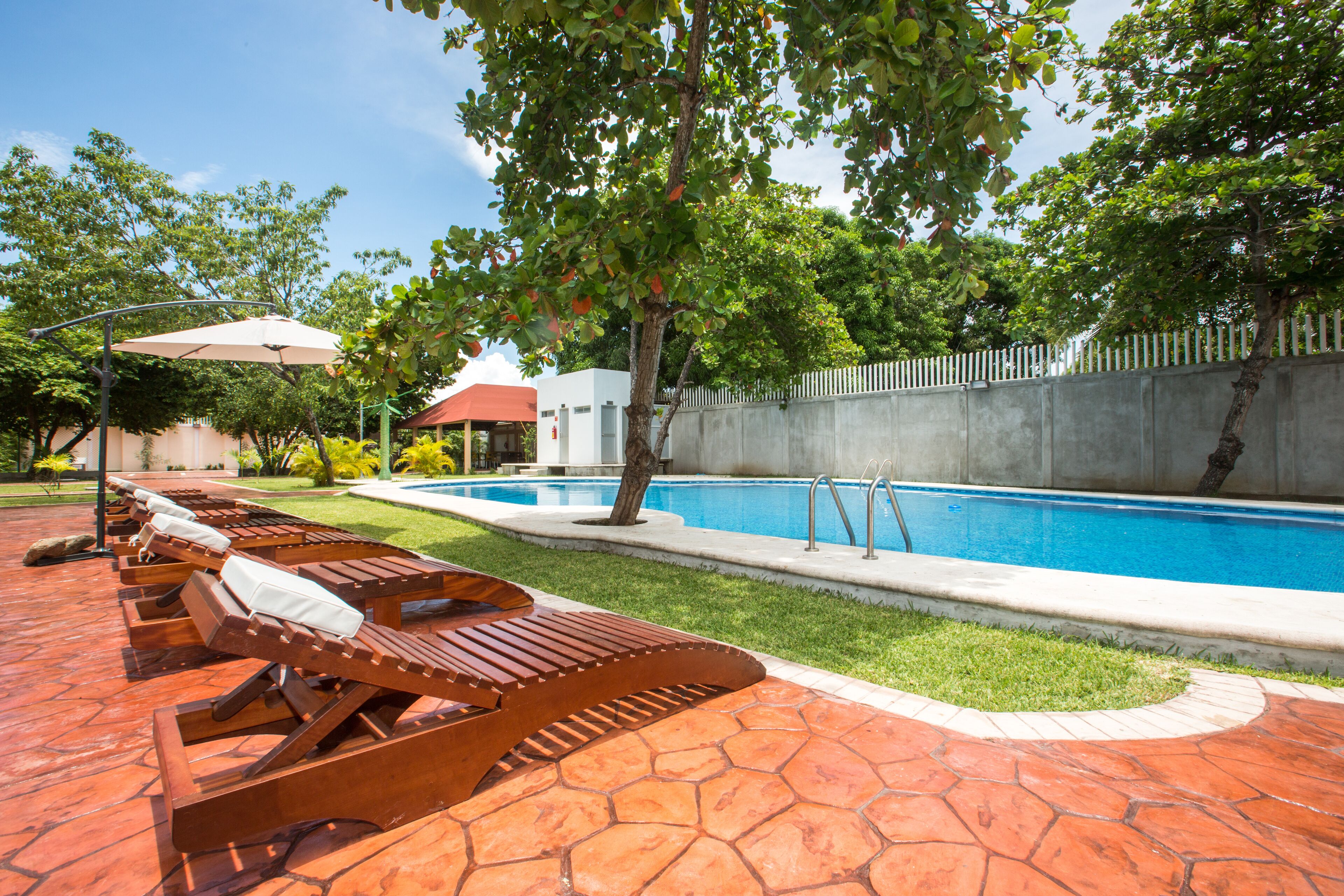 A poolside area with lounge chairs, a swimming pool, and a white fence.