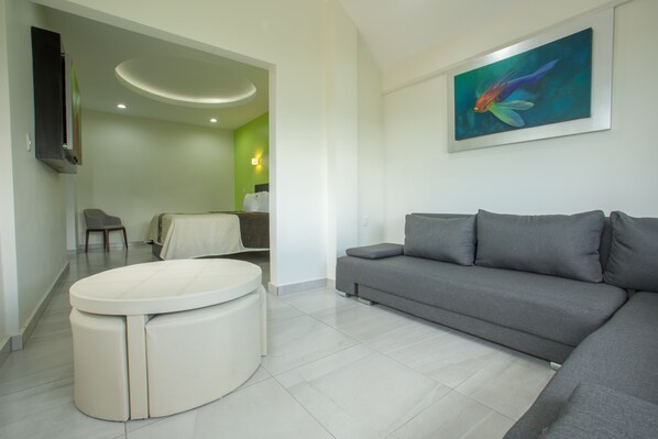 A modern living room with a grey sofa, a round ottoman, a dining area with a chair, and a painting on the wall. - KO'OLEBIL (Tonalá)