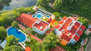 An aerial view of a residential area with a swimming pool, a red-roofed building, and lush greenery.