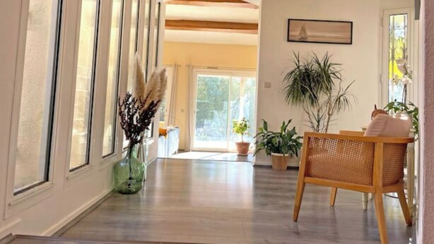 A spacious hallway with wooden flooring, large windows, and a rattan chair. - Architect-designed villa with swimming pool and large garden (Marseille)