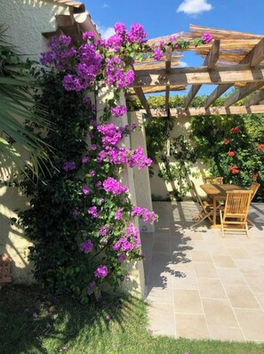 A patio area with a pergola, a wooden table and chairs, and a wall covered with purple flowers. - Architect-designed villa with a pool and large garden (Marseille)