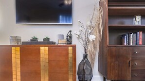 A reception area with a wooden reception desk, a large flat-screen TV mounted on the wall, a bookshelf with books, and a vase with dried plants.