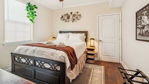 A bedroom with a bed, a ceiling fan, a wall-mounted plant, a decorative wall piece, a bedside table with a lamp, and a door.