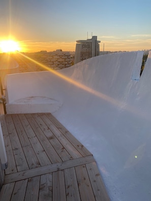 A rooftop terrace with a wooden deck, a white wall, and a view of the city skyline at sunset. - 3 Pieces Arty au 14eme Étage Vue Panoramique ! (Créteil)