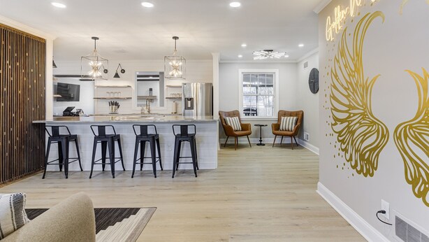 A modern kitchen with a central island, bar stools, pendant lighting, and a dining area with chairs and a table.