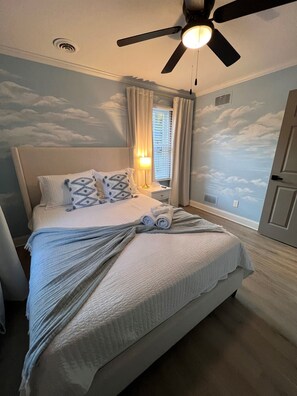 A bedroom with a bed, a ceiling fan, a nightstand, and a window with curtains.