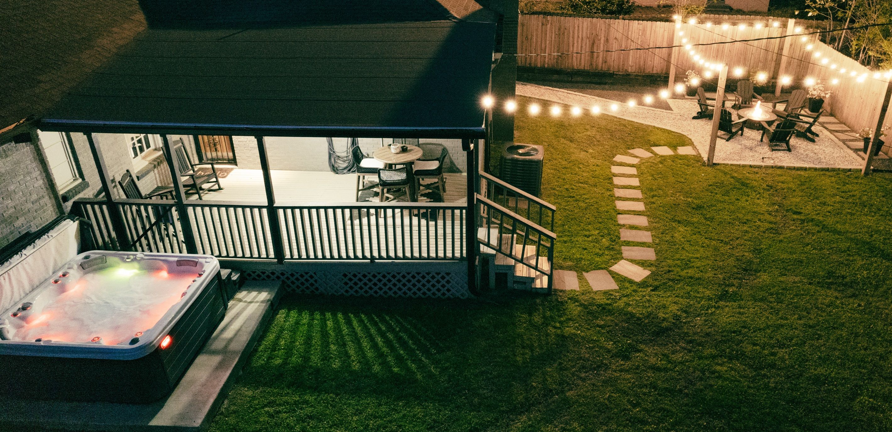 A backyard with a hot tub, a covered patio, and string lights.