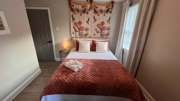 A neatly made bed with a red quilt, a bedside lamp, and a floral curtain.