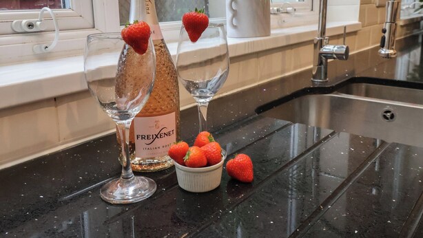 En köksbänk med två flaskor champagne, två glas och en skål med jordgubbar.