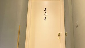 A closed door with the number 404 on it, a wooden stick leaning against the wall, and a light switch on the wall. - Base Napoli Plebiscito (Naples)
