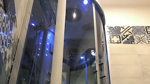 A modern bathroom with a glass-enclosed shower, tiled walls, and a visible hand dryer. - Base Napoli Plebiscito (Naples)
