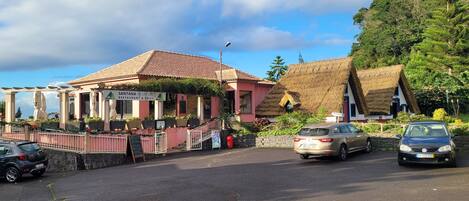 A restaurant with a red facade and a thatched roof, surrounded by lush greenery.