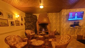 A cozy living room with wicker furniture, a fireplace, and a television displaying a sports event. - SLEEP AND GO - SANTANA IN NATURE B&B (Santana)