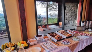 A breakfast buffet with various food items and beverages, set against a backdrop of a scenic view through large windows. - SLEEP AND GO - SANTANA IN NATURE B&B (Santana)