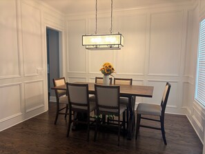Ein Esszimmer mit Holztisch und Stühlen, einer hängenden Leuchte und einer Vase mit Blumen.