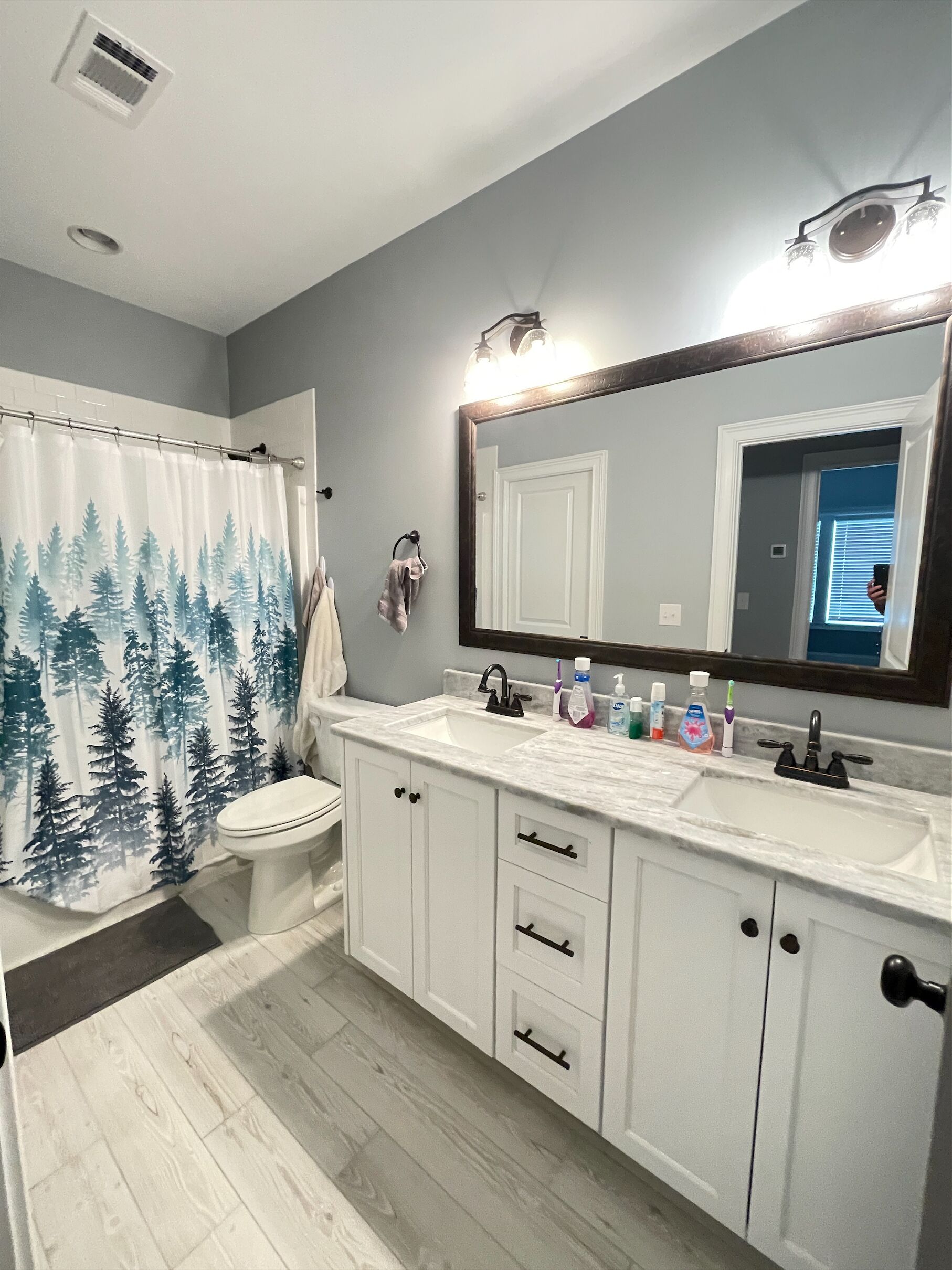 A bathroom with a shower curtain, toilet, sink, and cabinets.