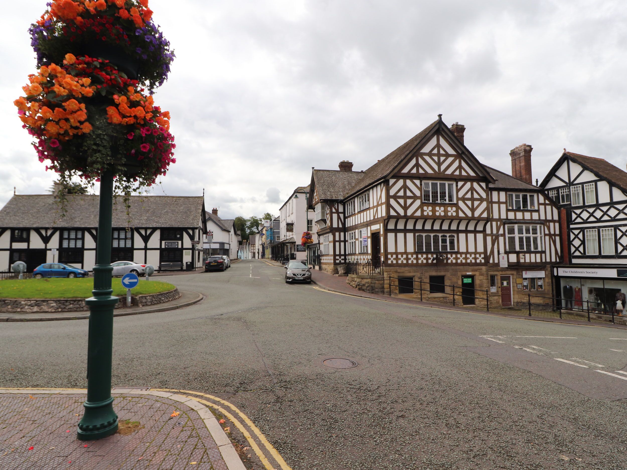 Una calle con edificios tradicionales de entramado de madera, una glorieta y una exhibición de flores.
