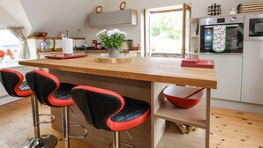 Una cocina moderna con una isla de madera, taburetes de bar rojos y negros, y vistas al exterior.