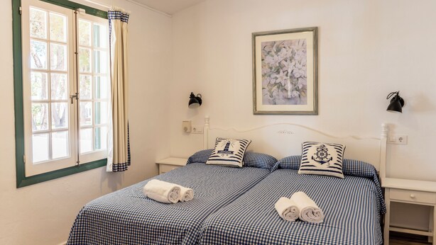 Une chambre avec deux lits, une literie à motifs à carreaux, une œuvre d’art florale encadrée et une fenêtre avec des rideaux.