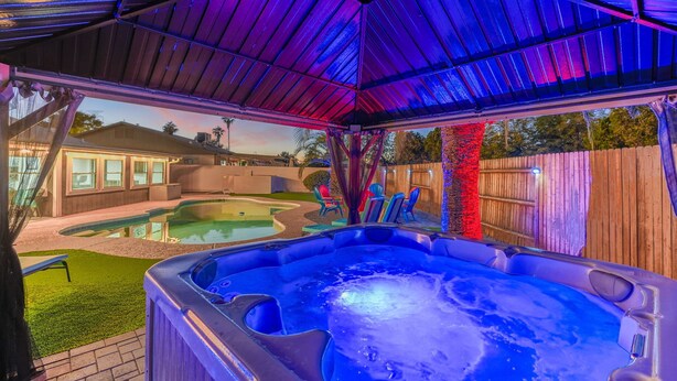 Un bain à remous sous un patio couvert, avec une piscine en arrière-plan.