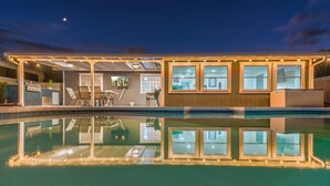 Un espace aménagé au bord de la piscine, avec un patio couvert, des sièges d’extérieur et un barbecue.