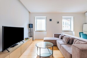 A modern living room with a flat-screen TV, a glass coffee table, a sofa, and two windows. -  2BR Chic&Bright com 120m2 em Campo de Ourique (Lisbon)