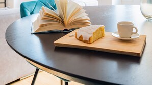 A round table with an open book, a slice of cake, and a cup of coffee. -  2BR Chic&Bright com 120m2 em Campo de Ourique (Lisbon)
