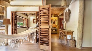 A hammock in a room with wooden floors, a dining table, and a view of greenery outside. - Sempre Vivo (Tibau do Sul)