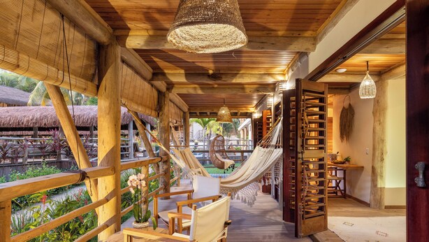 A wooden deck with a hammock, a chair, and a table with a vase of flowers. - Sempre Vivo (Tibau do Sul)