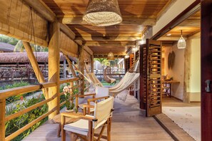 A wooden deck with a hammock, a chair, and a table with a vase of flowers. - Sempre Vivo (Tibau do Sul)