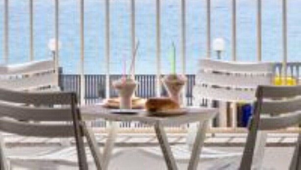Un balcon avec une table et des chaises, donnant sur une étendue d’eau.