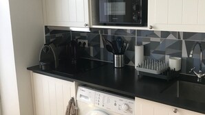 Una cocina compacta con muebles blancos, lavadora Bosch, microondas y cafetera.
