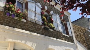 Un edificio con paredes exteriores de piedra y enlucido, contraventanas blancas y jardineras en el piso superior.