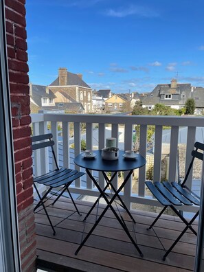 Une terrasse en bois avec une table ronde et deux chaises, donnant sur un quartier résidentiel avec des maisons et un ciel dégagé.