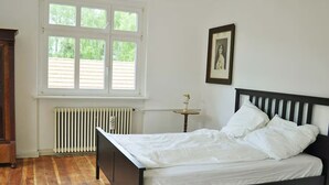 A bedroom with a wooden bed, a radiator, a window with blinds, and a framed picture on the wall. - VILLA FOREST & LAKES near Berlin - Country villa with horses, fireplace & peace! (Marienwerder-Ruhlsdorf)
