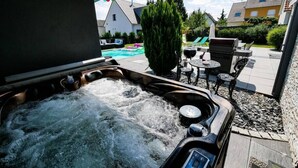 A hot tub with a control panel, surrounded by outdoor furniture and a swimming pool in the background. - Private heated pool and jacuzzi villa (Furdenheim)