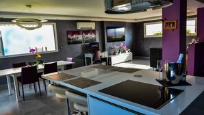 A modern kitchen with a central island, dining area, and a TV mounted on the wall. - Private heated pool and jacuzzi villa (Furdenheim)