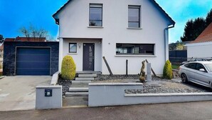 A modern two-story house with a garage, a front door, and a driveway leading to a parked car. - Private heated pool and jacuzzi villa (Furdenheim)