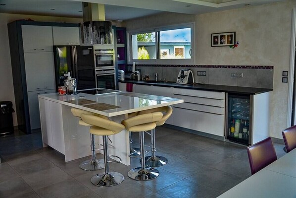 Une cuisine moderne dotée d’un îlot central, de deux tabourets de bar, d’appareils électroménagers en acier inoxydable et d’une fenêtre offrant une vue agréable.