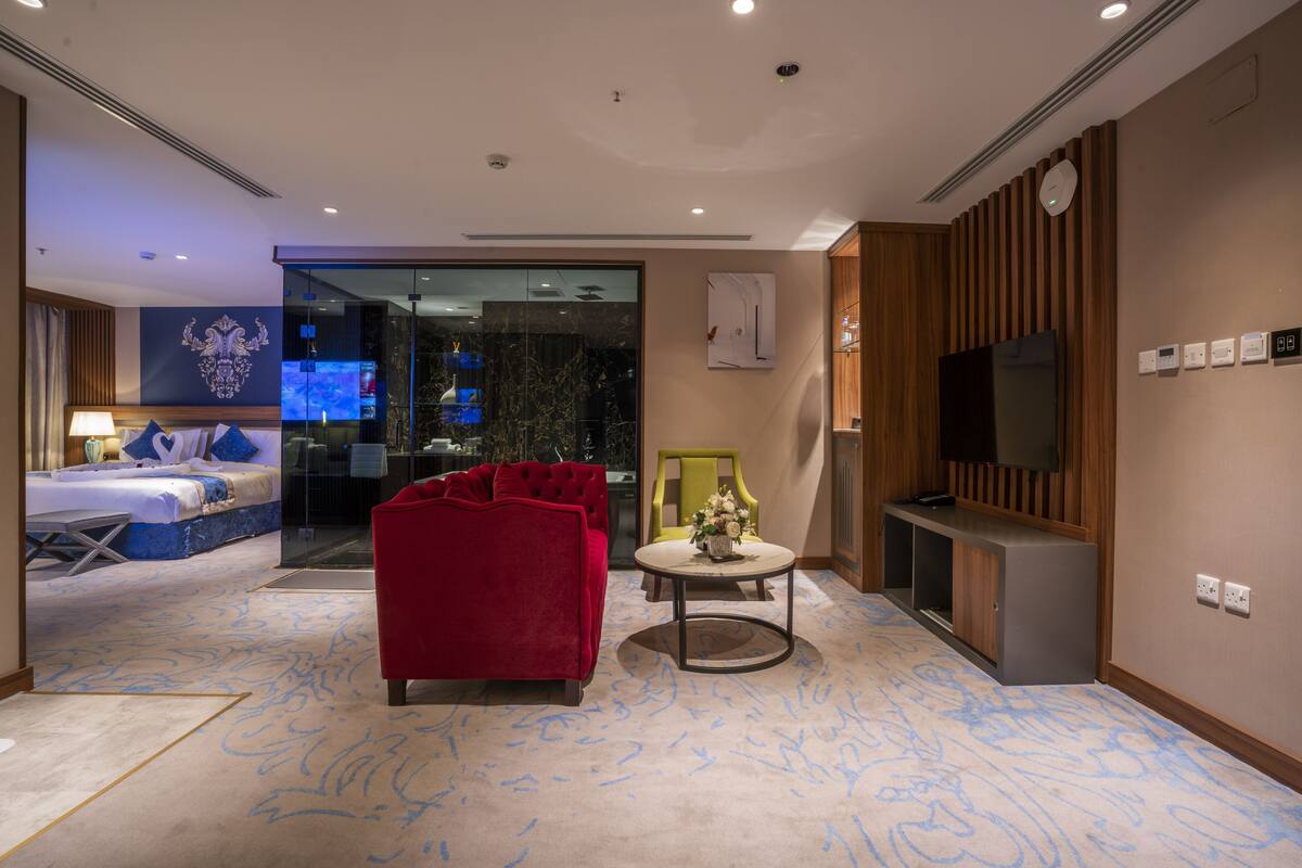 A modern hotel room with a red sofa, a small round table, a TV, and a large window.
