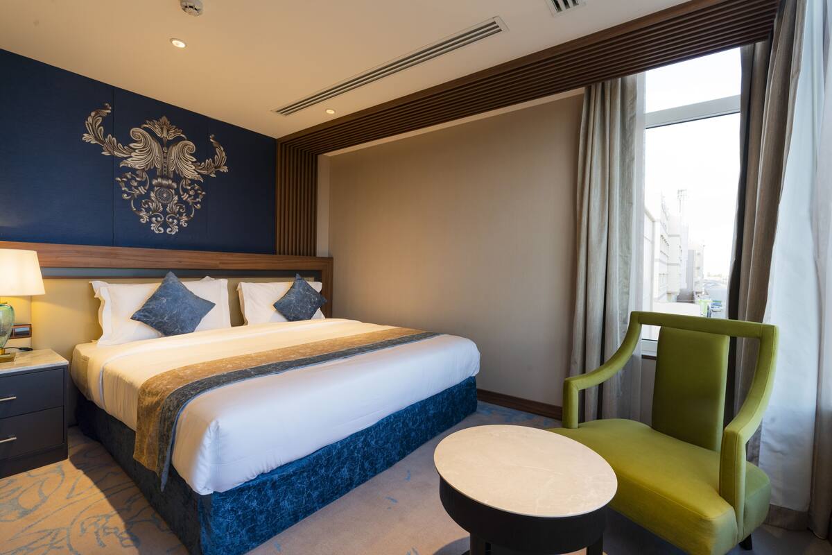 A hotel room with a large bed, a green armchair, a small round table, and a decorative wall piece.