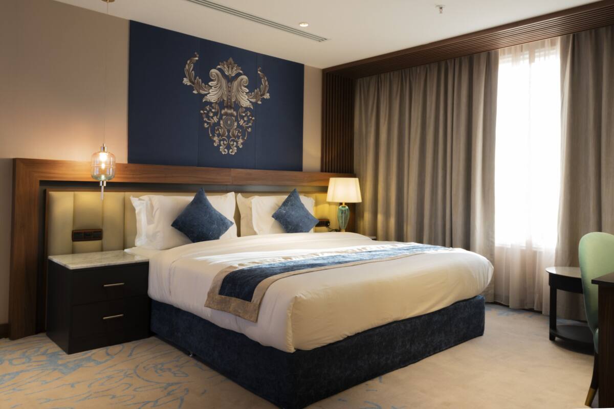 A hotel room with a large bed, a nightstand, a lamp, and a chair.