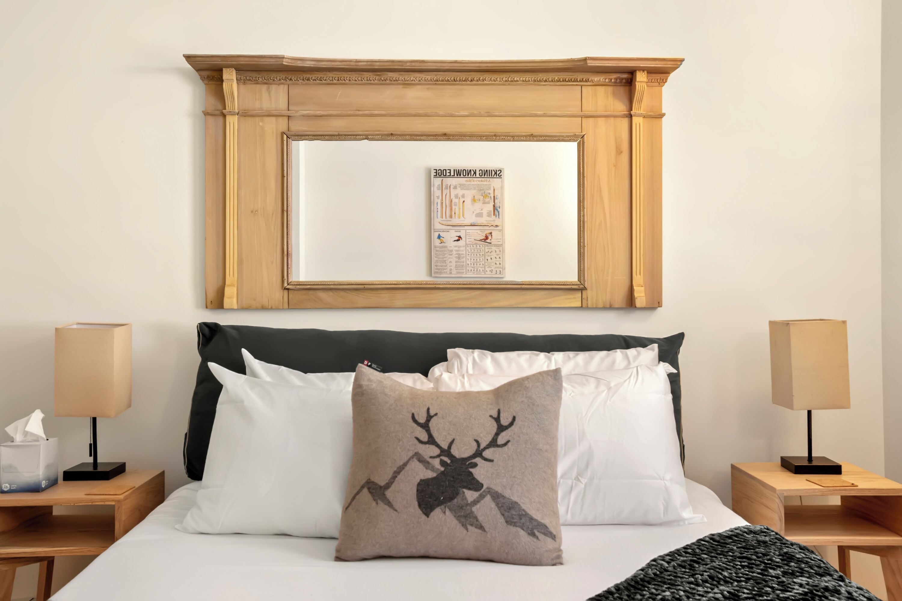 Uma cama bem arrumada com roupa de cama branca e preta, um travesseiro com tema de veado e um cartaz educativo emoldurado acima.