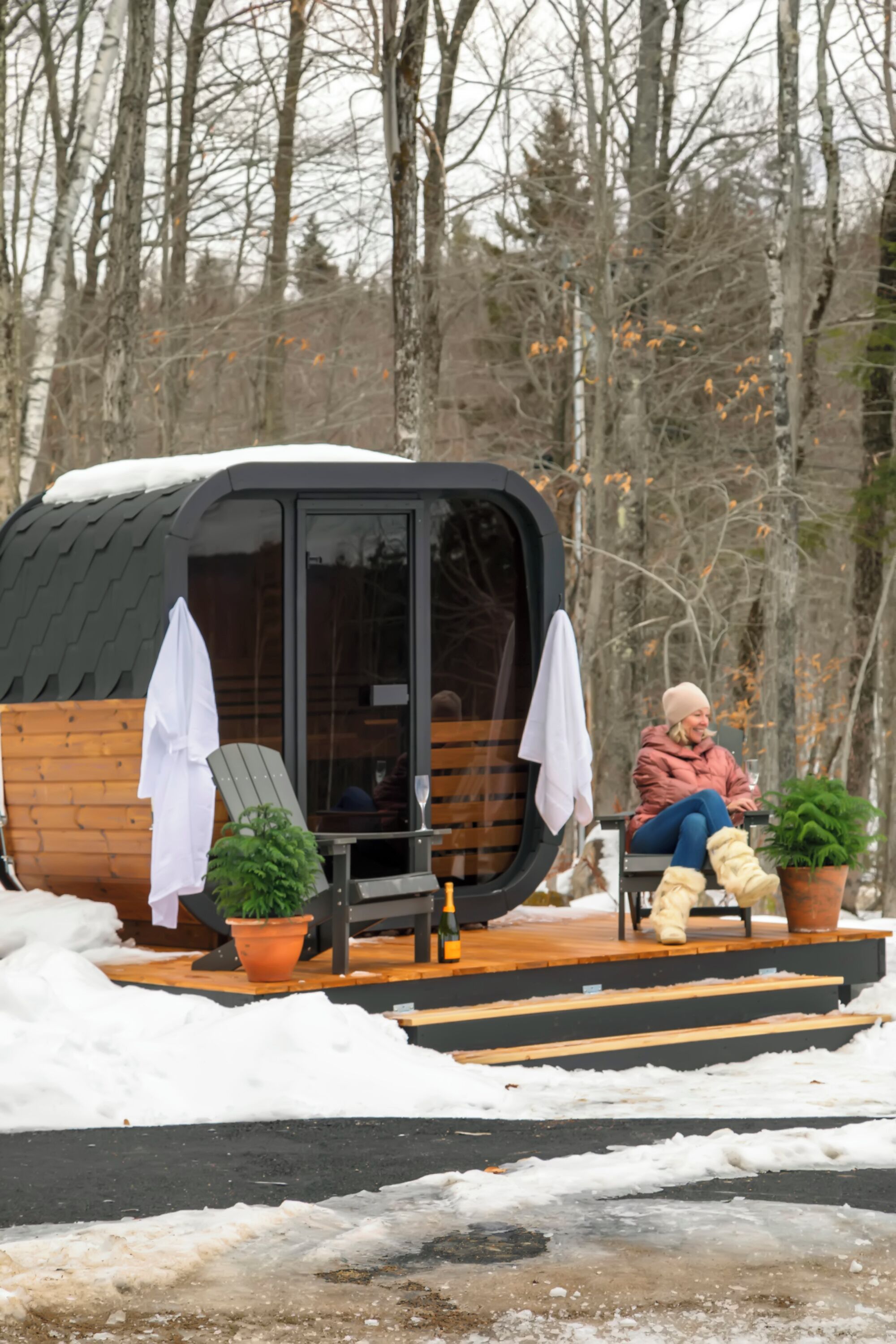 Una cabaña con terraza de madera, puerta de cristal y una persona sentada en una silla.
