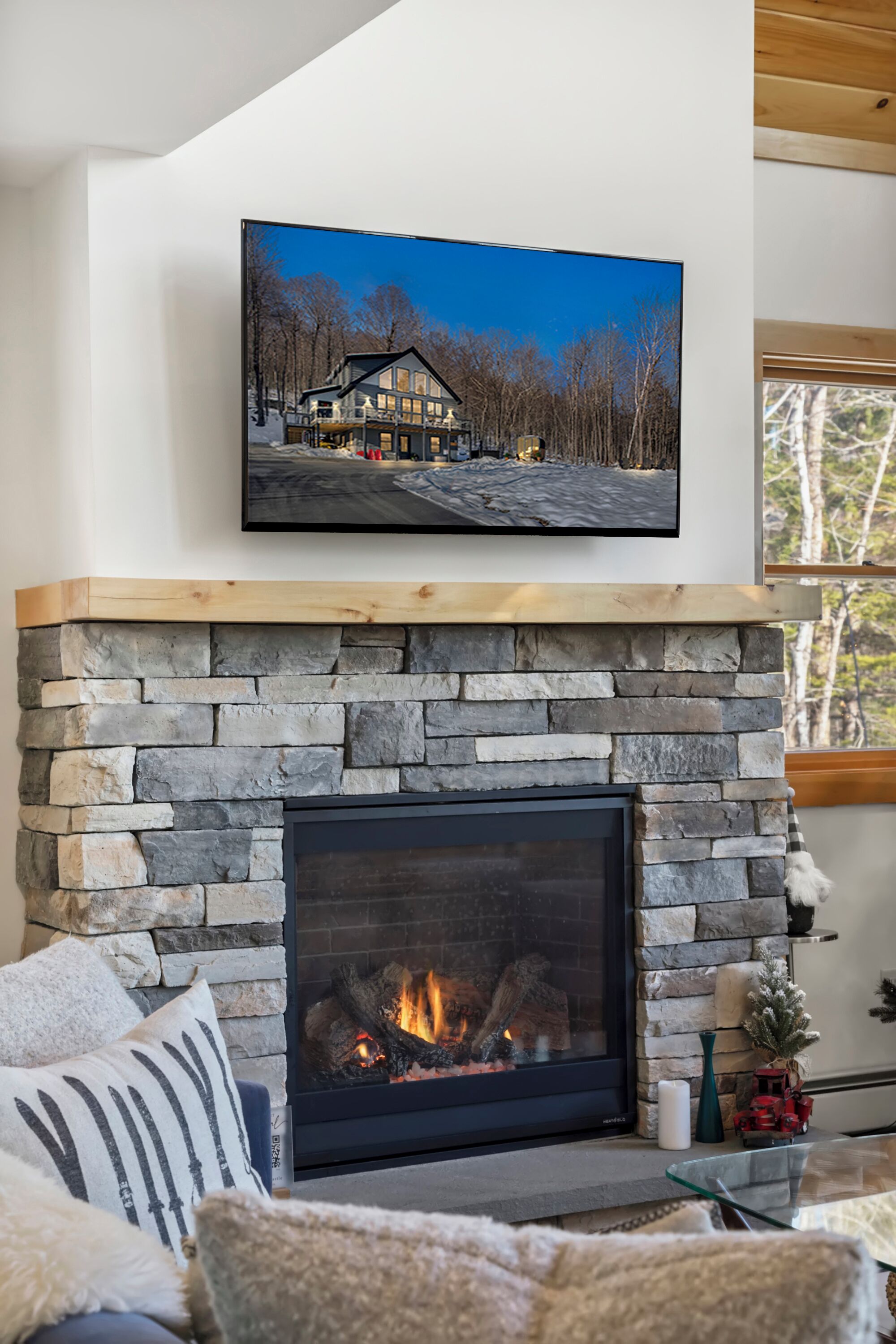 Una sala de estar acogedora con chimenea de piedra, un televisor montado encima y una zona de estar cómoda con cojines.