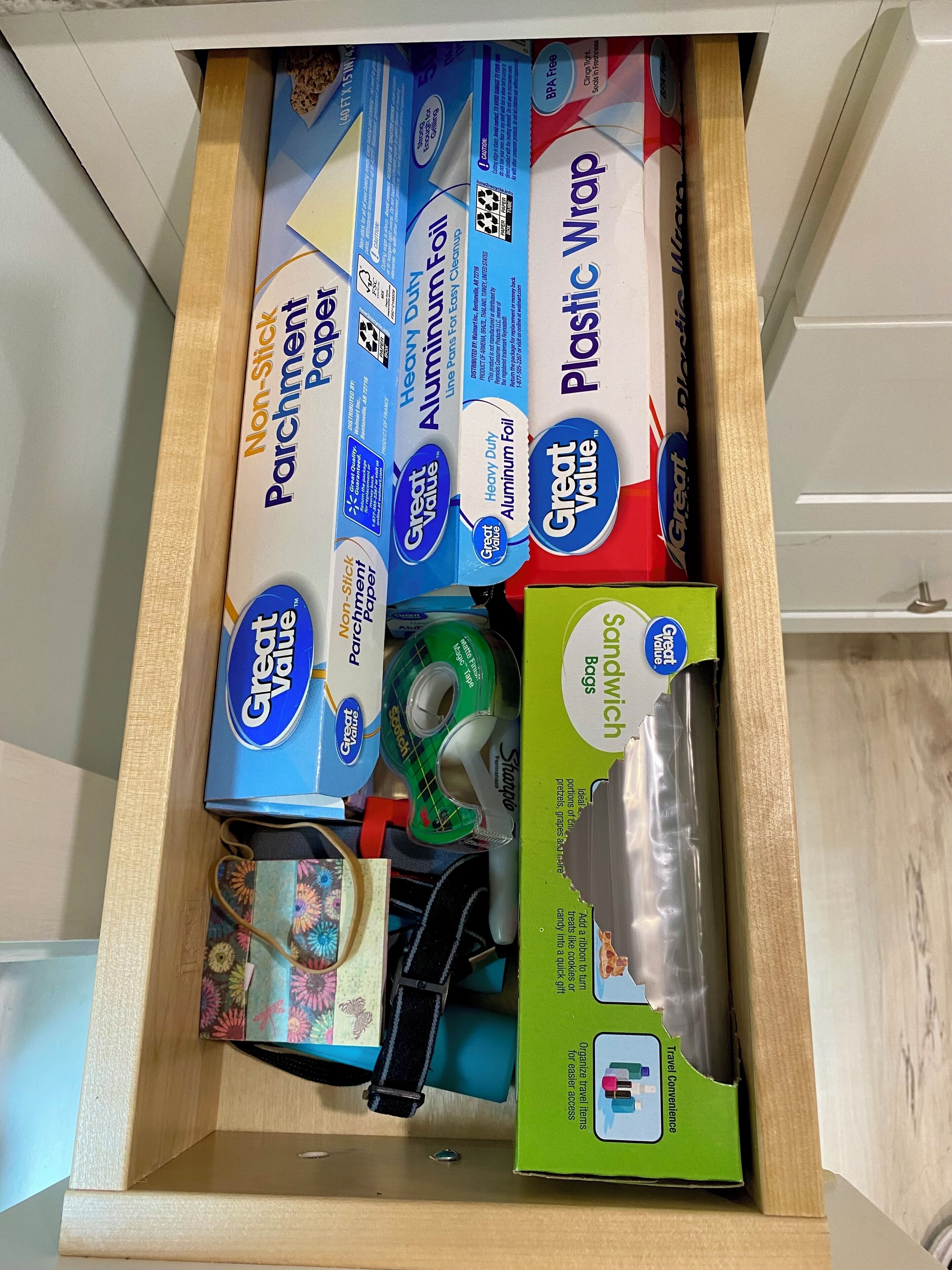 A drawer containing various office supplies including non-stick parchment paper, heavy-duty aluminum foil, plastic wrap, and sandwich bags.